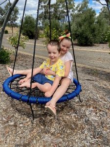 Two children are smiling, playing on a swing