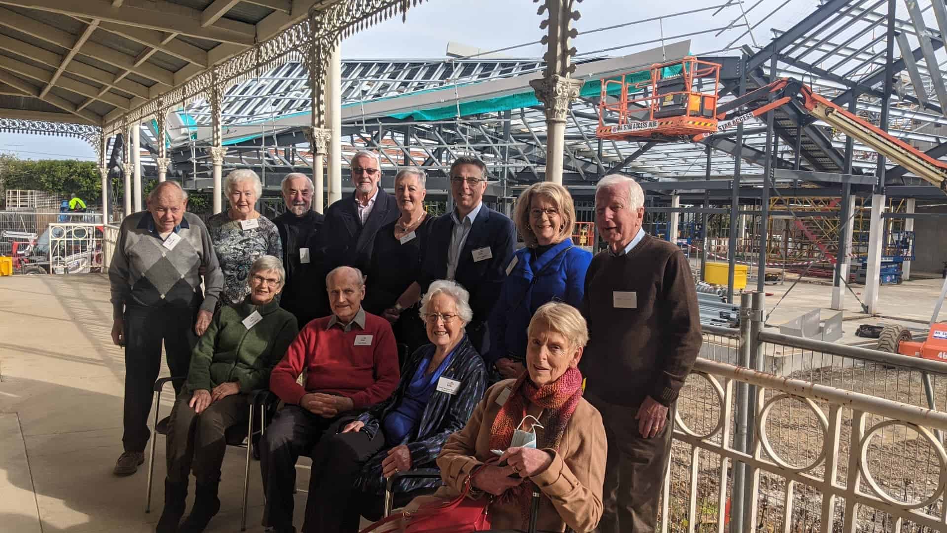 A group of adults are seated on the balcony of Very Special Kids, they are smiling at the camera. In the background construction of the new hospice can be seen.
