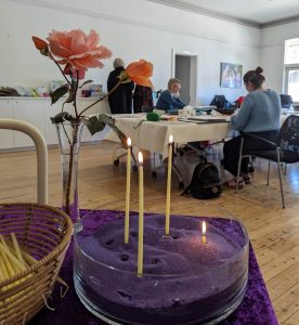 In the distance, adults are sitting at a table doing scrapbooking. In the foreground there are lit taper candles and roses in a vase.