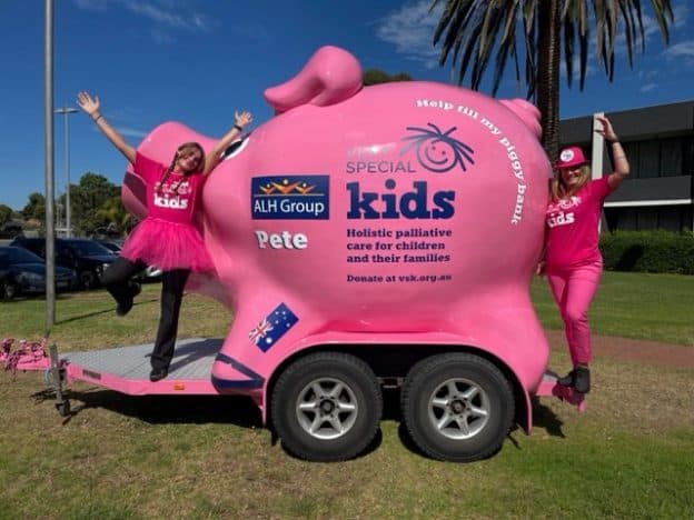 Two adults are dressed up in pink costumes and posing with a giant Very Special Kids piggy bank.