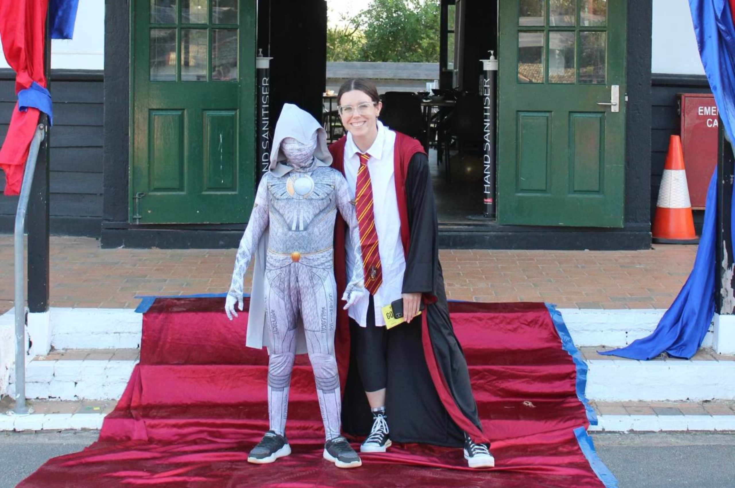 An adult woman and a young boy are standing on steps on a red carpet. They are dressed in Harry Potter costumes and smiling at the camera.