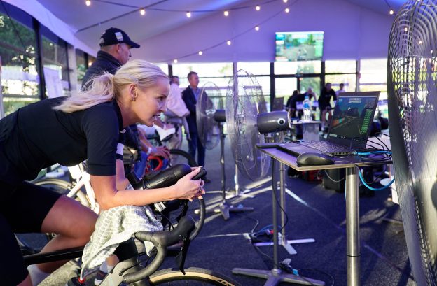 A woman is riding a bike indoors, there are other riders in the background.