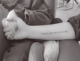 Image of a tattoo on the inside of a woman's arm, reading "I am his voice and he is my heart".