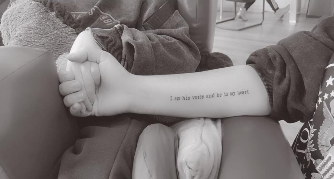 Image of a tattoo on the inside of a woman's arm, reading "I am his voice and he is my heart".