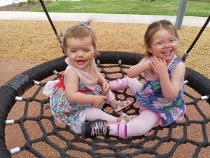 Two young girls are sitting on a swing smiling at the camera.