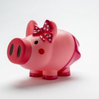 A piggy bank decorated with blushing cheeks and a spotted bow on it's head.