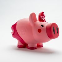 A piggy bank decorated with blushing cheeks and a spotted bow on it's head.