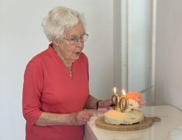 An older woman is blowing out candles on her birthday cake. They indicate that she is turning 90.