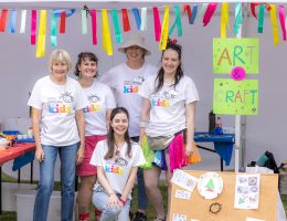 A group of adults are standing in a marquee, they are all wearing Very Special Kids t-shirts and smiling at the camera. There is a sign reading 'Art and Crafts'
